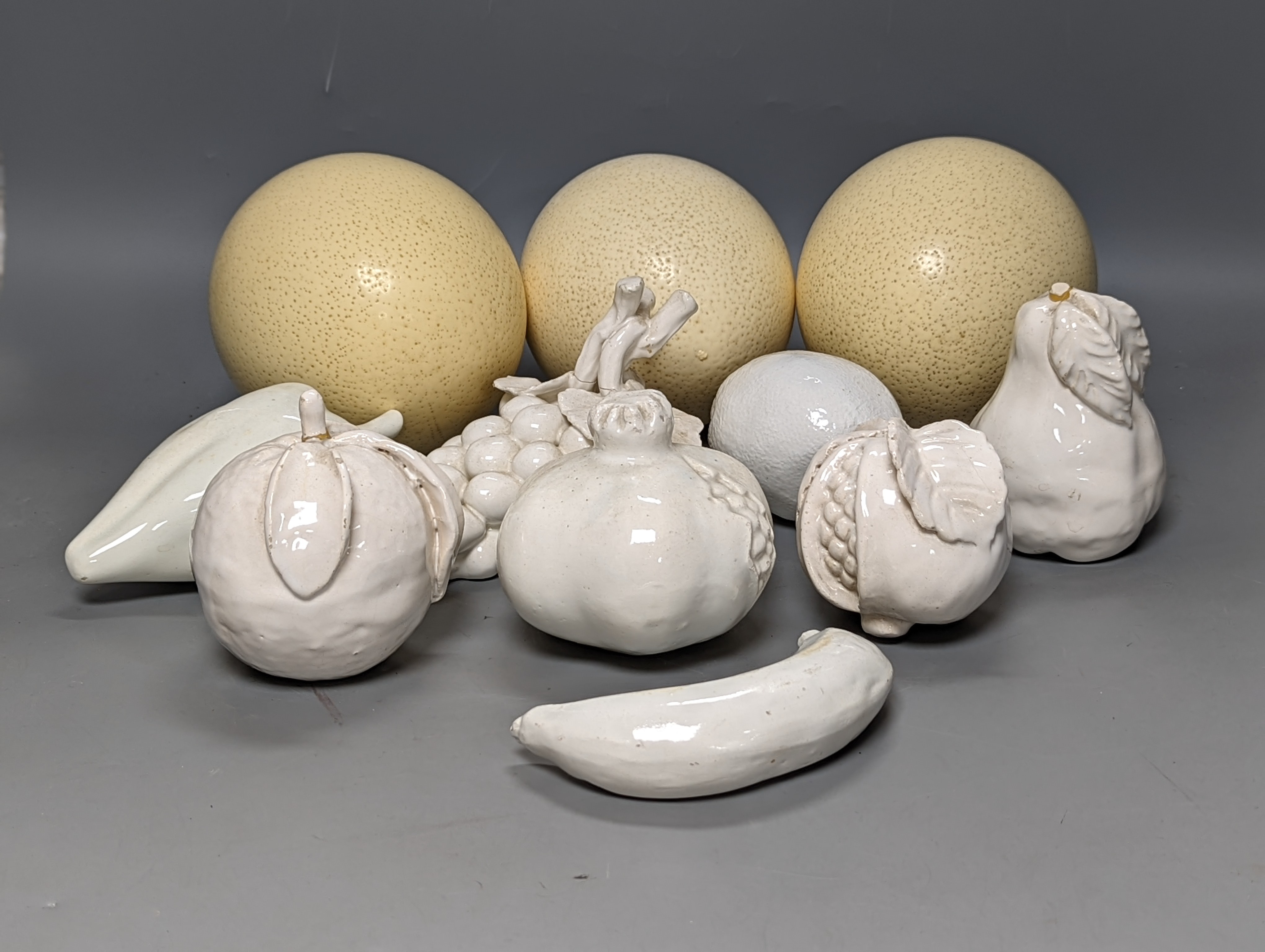 A decorative collection of tin glazed model fruits, together with three ostrich eggs